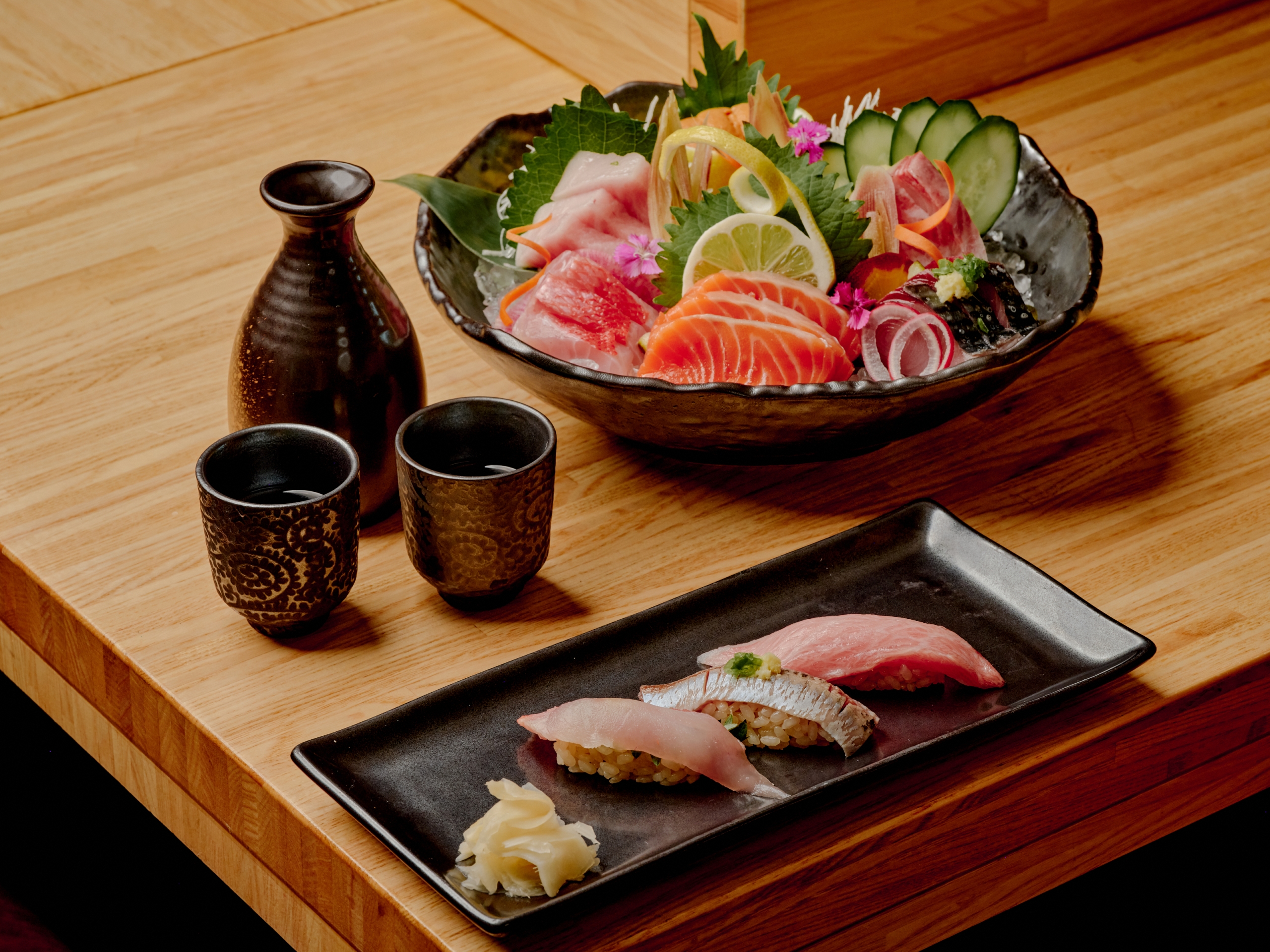 a sashimi platter and nigiri platter with a bottle of sake next to it